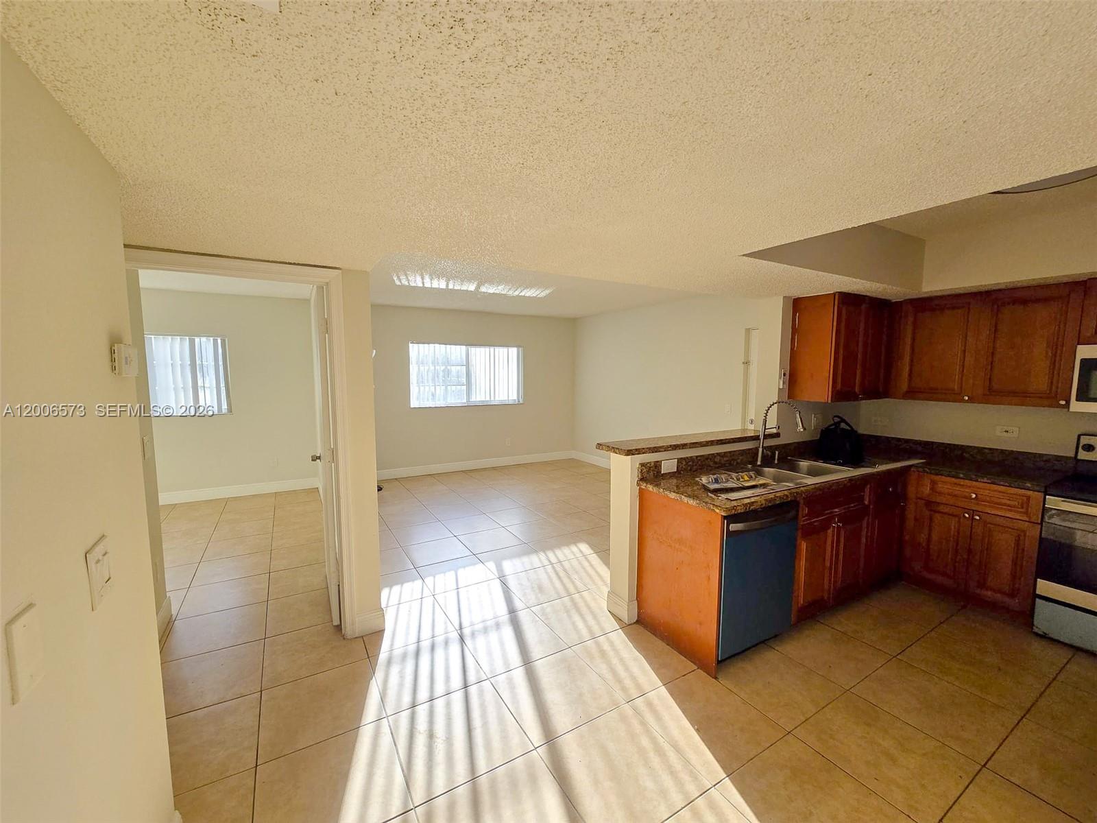A kitchen with wood cabinets and granite countertops opens into a tiled living area — 3690 N 56th Ave # 912, Hollywood FL 33021, HOLLYWOOD, FL