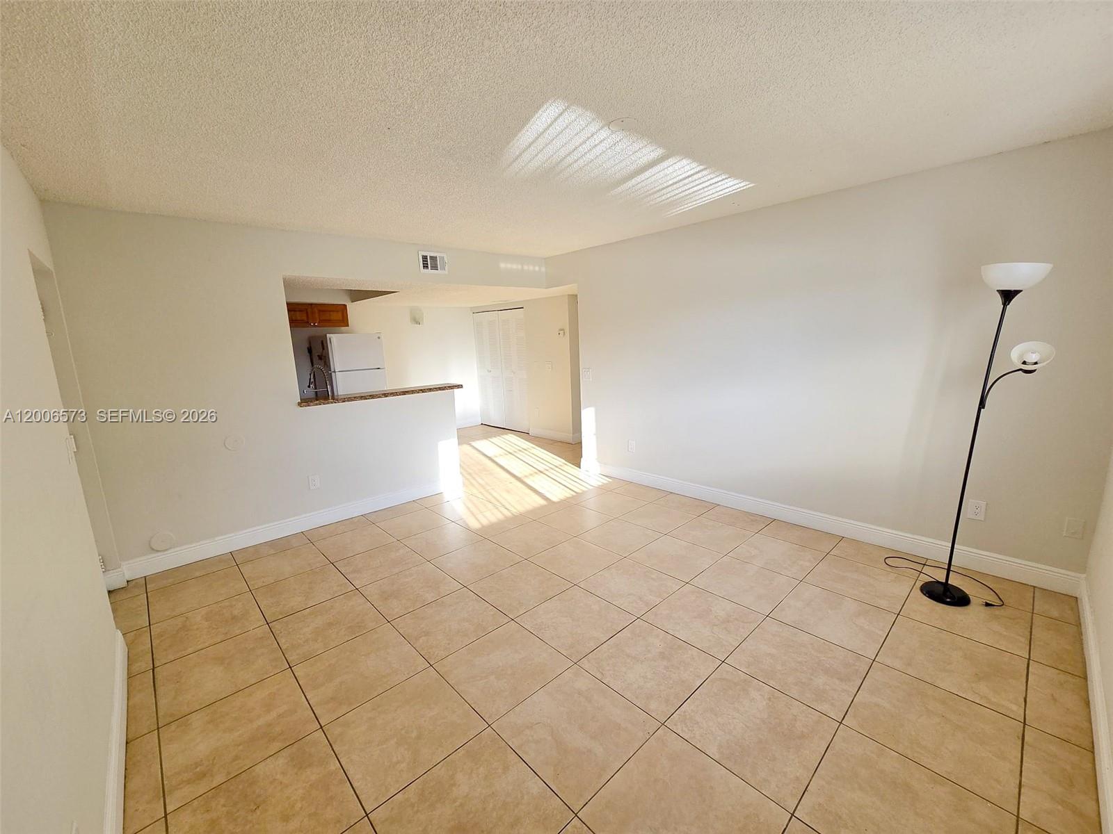 An empty living room features beige tile flooring, white walls, and an open kitchen pass-through — 3690 N 56th Ave # 912, Hollywood FL 33021, HOLLYWOOD, FL