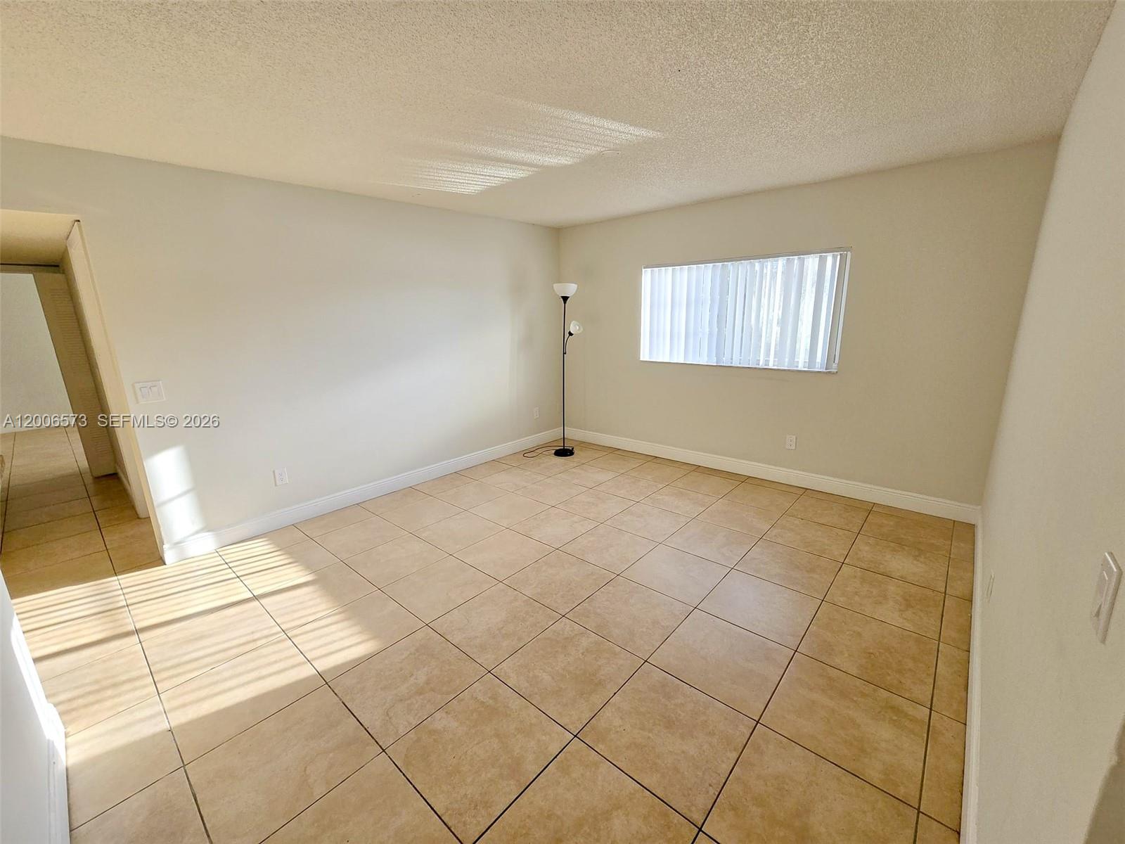 An empty room features beige tile flooring, light-colored walls, and a single floor lamp — 3690 N 56th Ave # 912, Hollywood FL 33021, HOLLYWOOD, FL