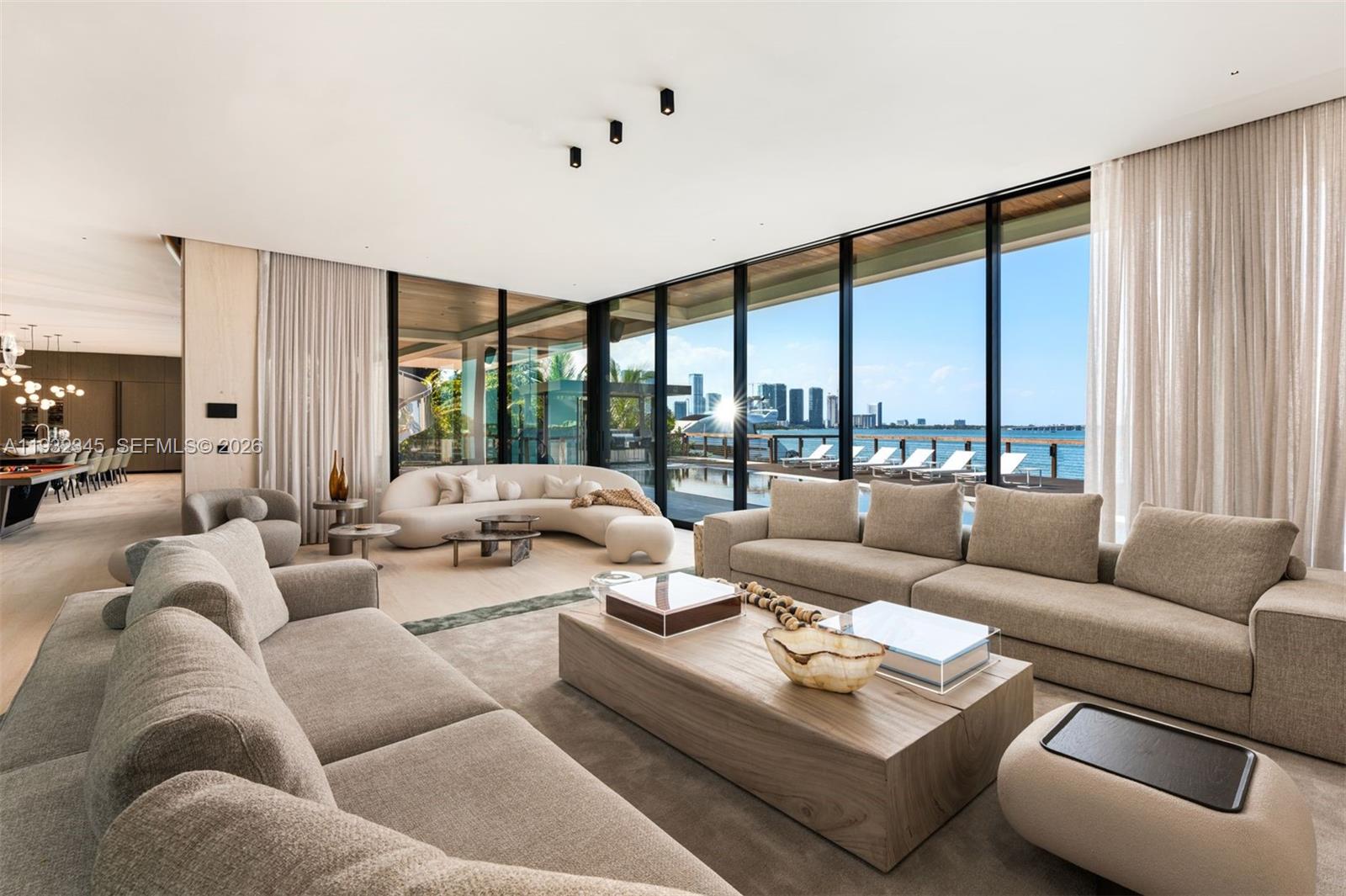 A modern living room features plush beige sofas, a wooden coffee table, and floor-to-ceiling windows — 1413 N Venetian Way, Miami FL 33139, MIAMI, FL