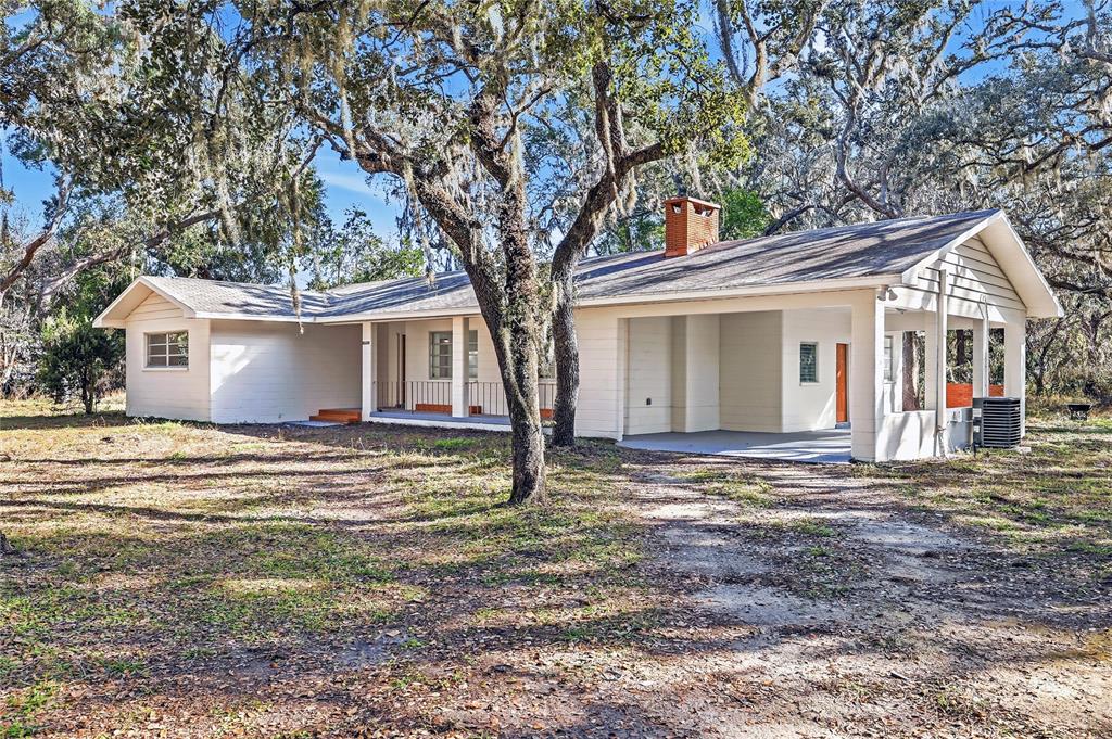 A single-story house with a brick chimney, covered porch, and carport under large oak trees — 34582 ORCHID PARKWAY, DADE CITY, FL