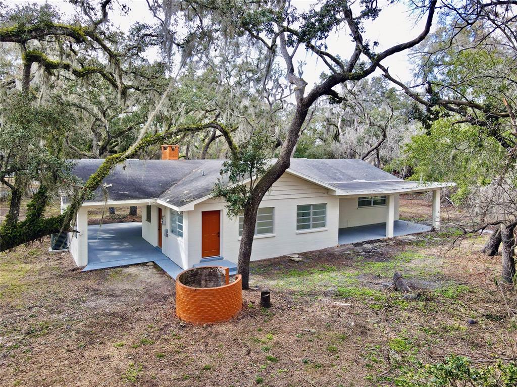 A single-story house with a carport, orange door, and brick well in a wooded yard — 34582 ORCHID PARKWAY, DADE CITY, FL