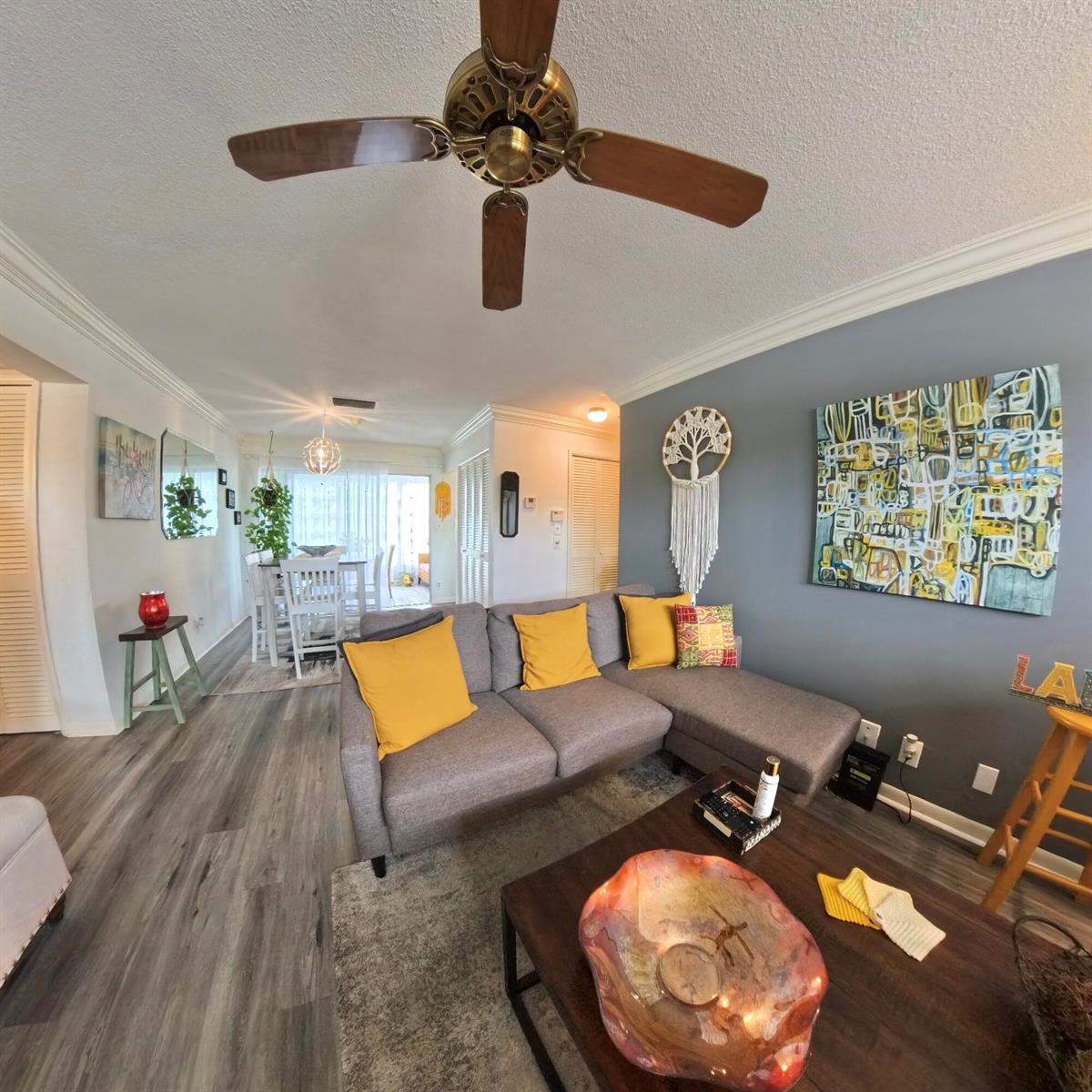 A living room features a grey sectional sofa, yellow pillows, and a large abstract painting — 4100 Crystal Lake Drive # 209, Pompano Beach FL 33064, POMPANO BEACH, FL