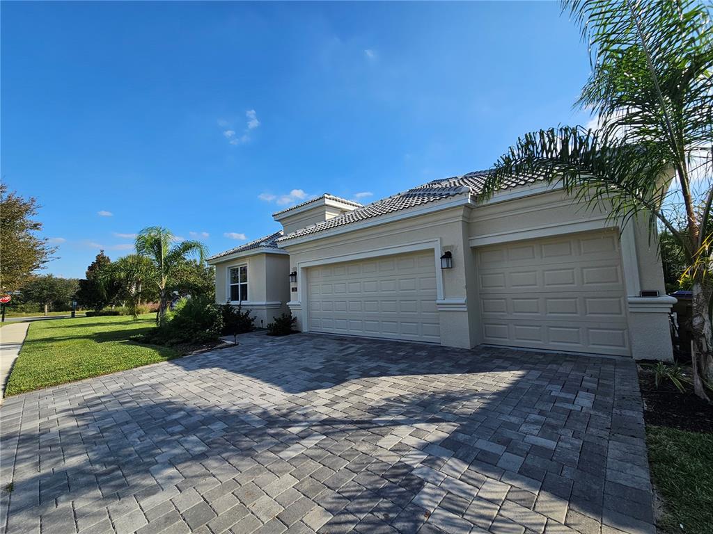 A beige house with a three-car garage and a paved driveway under a blue sky — 1351 OLYMPIC CLUB BOULEVARD, CHAMPIONS GATE, FL