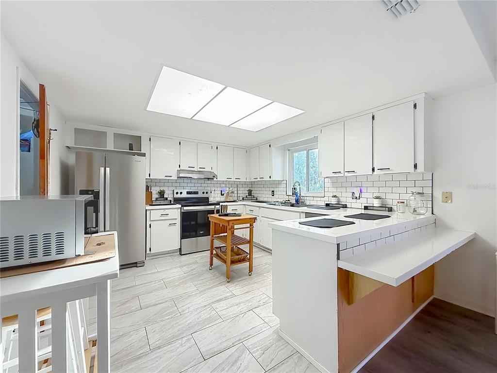 A kitchen features white cabinets, stainless steel appliances, a subway tile backsplash, and tile flooring — 1975 N SCENIC WAY, CRYSTAL RIVER, FL