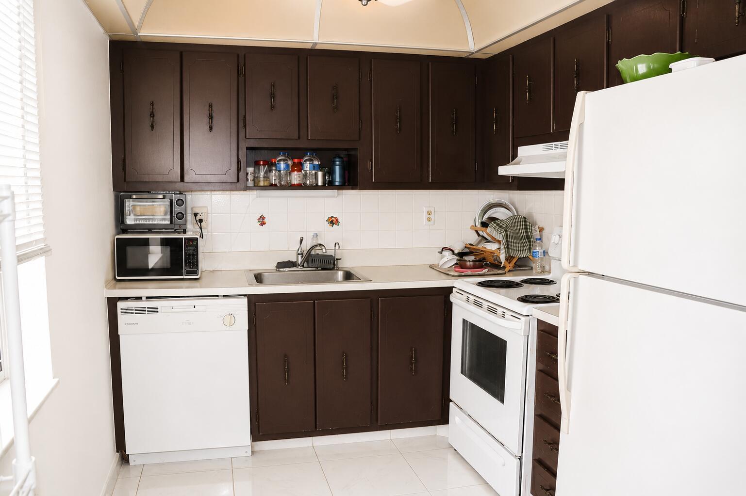 A kitchen features dark brown cabinets, white appliances, a tiled backsplash, and light-colored floor tiles — 321 Burgundy G, Delray Beach FL 33484, DELRAY BEACH, FL