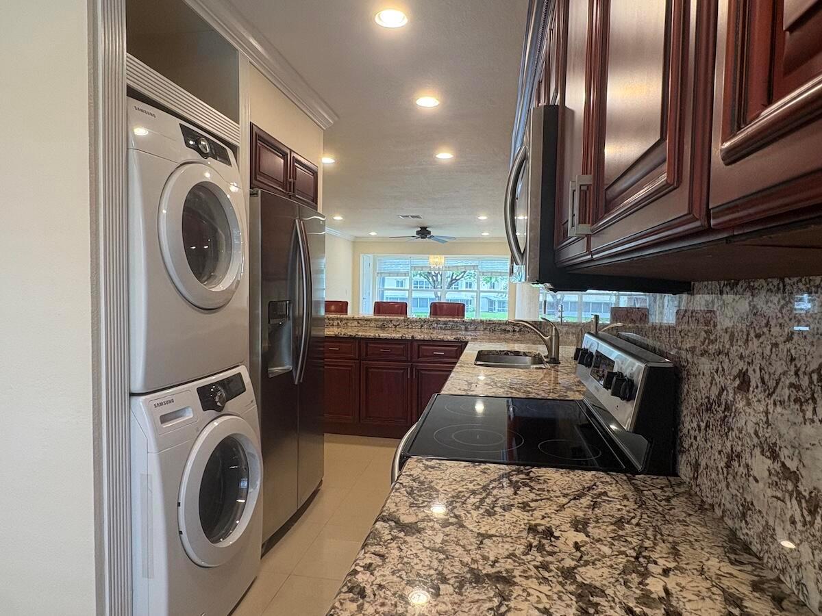 A kitchen features granite countertops, dark wood cabinetry, and a stacked washer and dryer unit — 1441 NW 19th Terrace # 201, Delray Beach FL 33445, DELRAY BEACH, FL