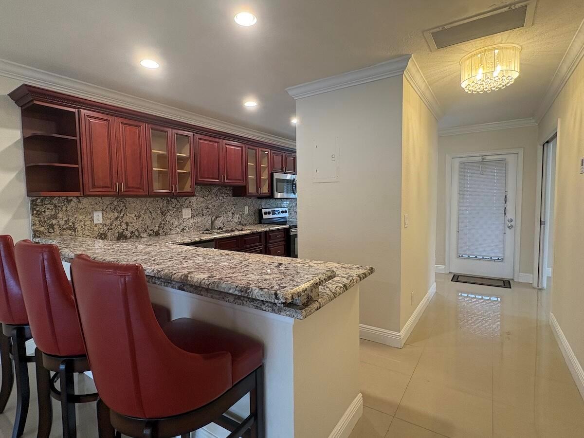 A kitchen with cherry wood cabinets, granite countertops, and a breakfast bar with red stools — 1441 NW 19th Terrace # 201, Delray Beach FL 33445, DELRAY BEACH, FL