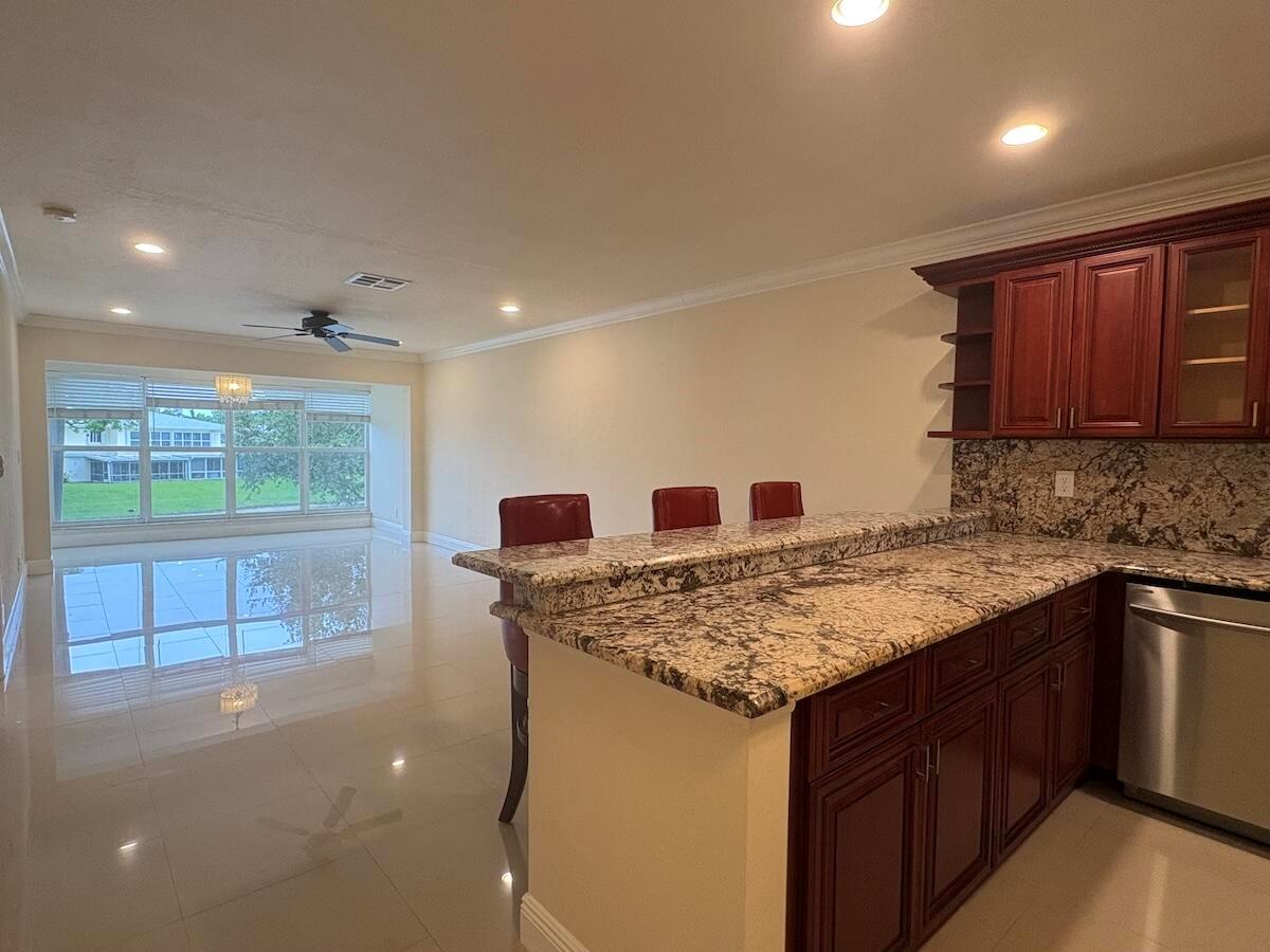 A kitchen with granite countertops and dark wood cabinets overlooks a bright, open living area — 1441 NW 19th Terrace # 201, Delray Beach FL 33445, DELRAY BEACH, FL