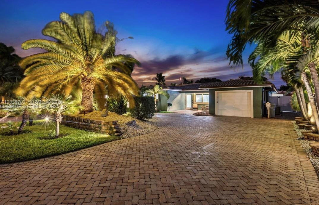 A paved driveway leads to a single-story house with a garage and illuminated palm trees — 2580 SE 2nd Ct, Pompano Beach FL 33062, POMPANO BEACH, FL