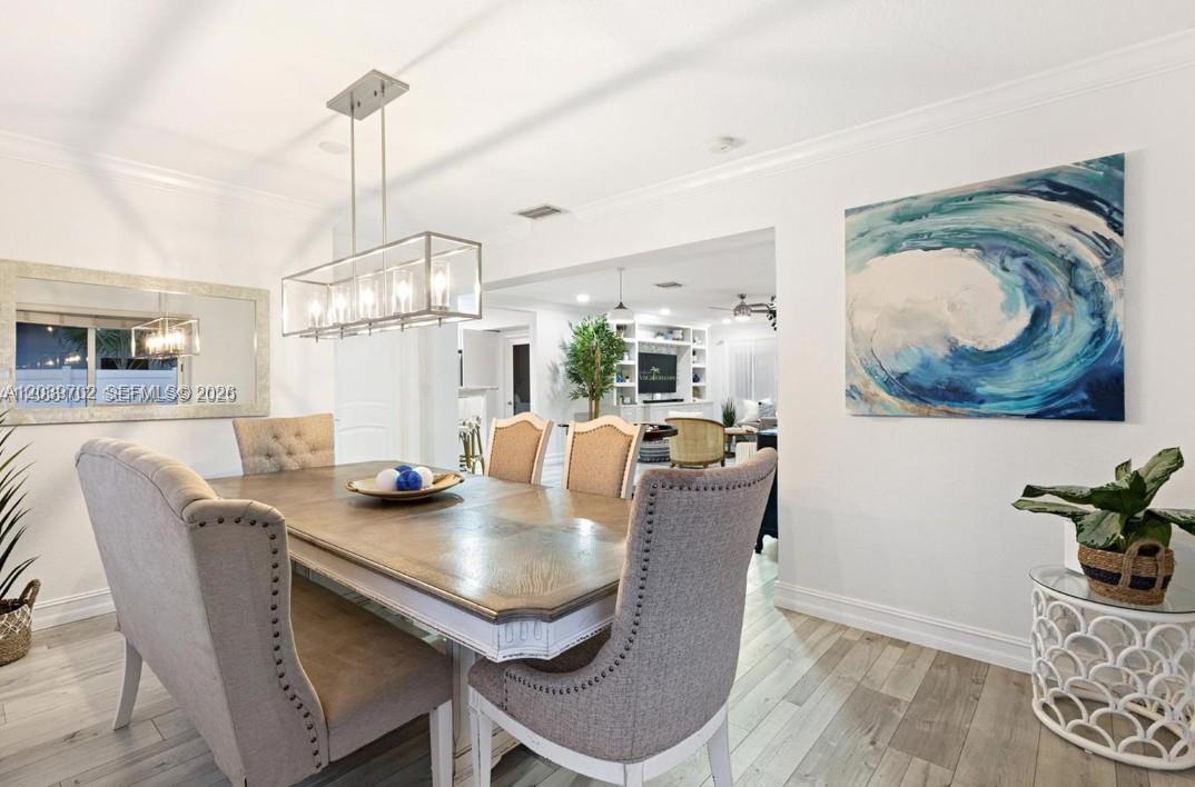 A dining room features a wooden table, upholstered chairs, a rectangular chandelier, and wall art — 2580 SE 2nd Ct, Pompano Beach FL 33062, POMPANO BEACH, FL