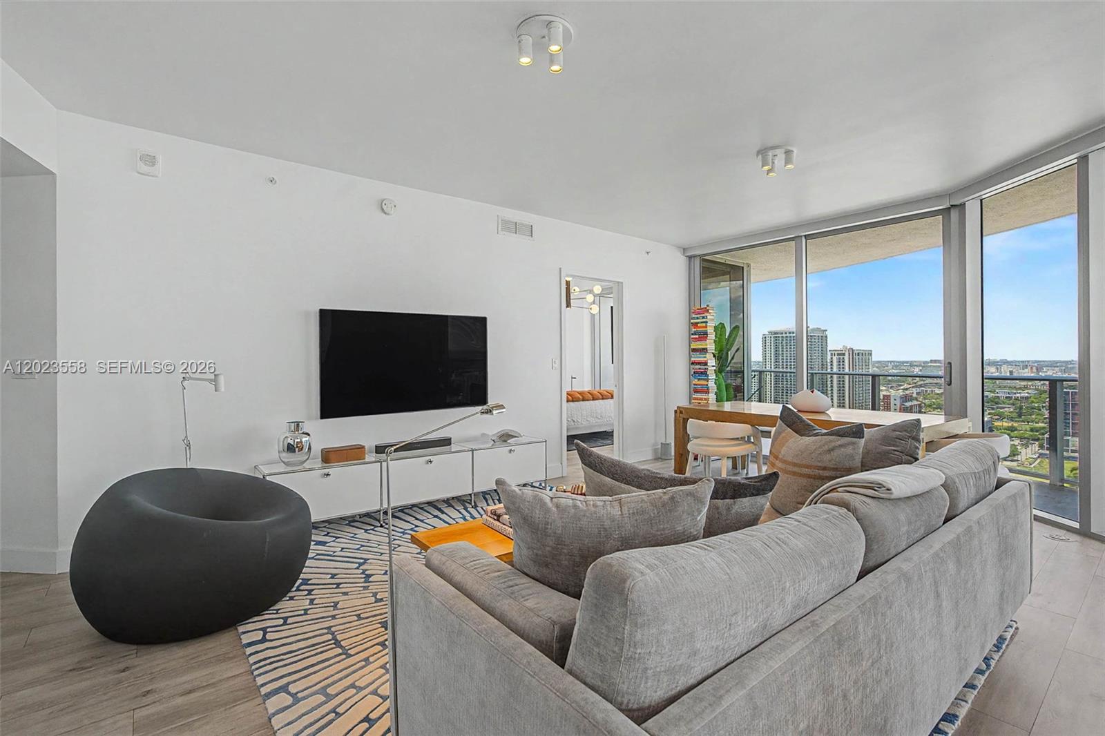 A modern living room features a grey sofa, a patterned rug, and floor-to-ceiling windows — 488 NE 18th St # 3101, Miami FL 33132, MIAMI, FL