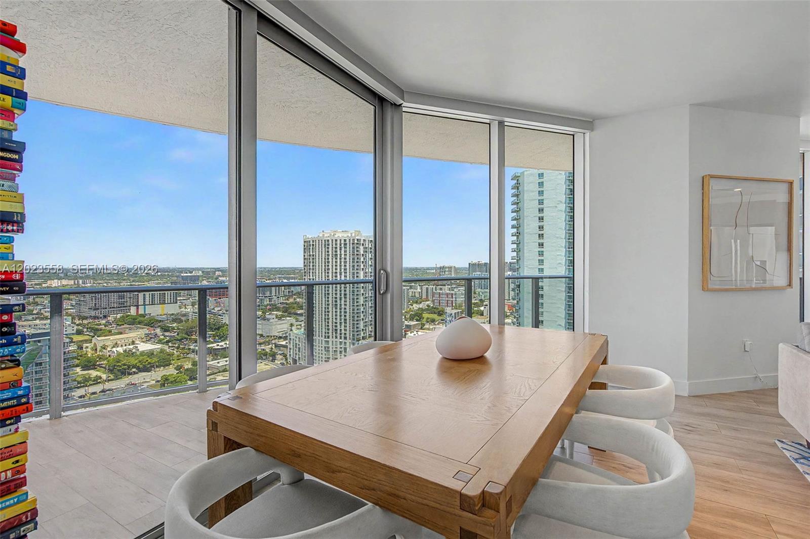 A dining area features a wooden table, white chairs, and floor-to-ceiling windows overlooking a city — 488 NE 18th St # 3101, Miami FL 33132, MIAMI, FL