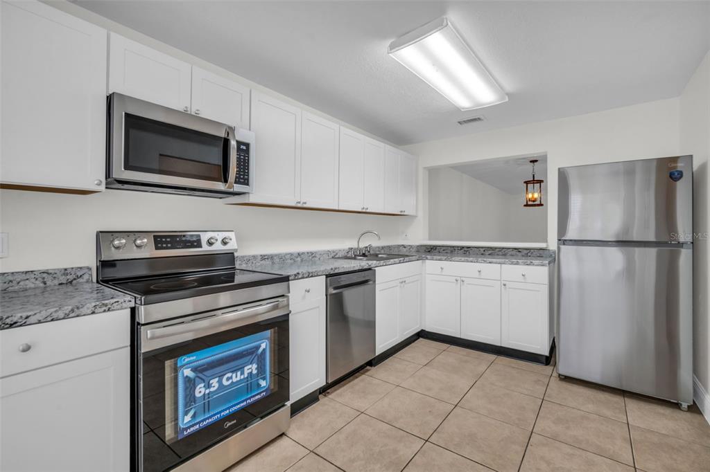 A kitchen with white cabinets, stainless steel appliances, and granite countertops over tile flooring — 1610 NW 93RD AVENUE UNIT 303, HOLLYWOOD, FL