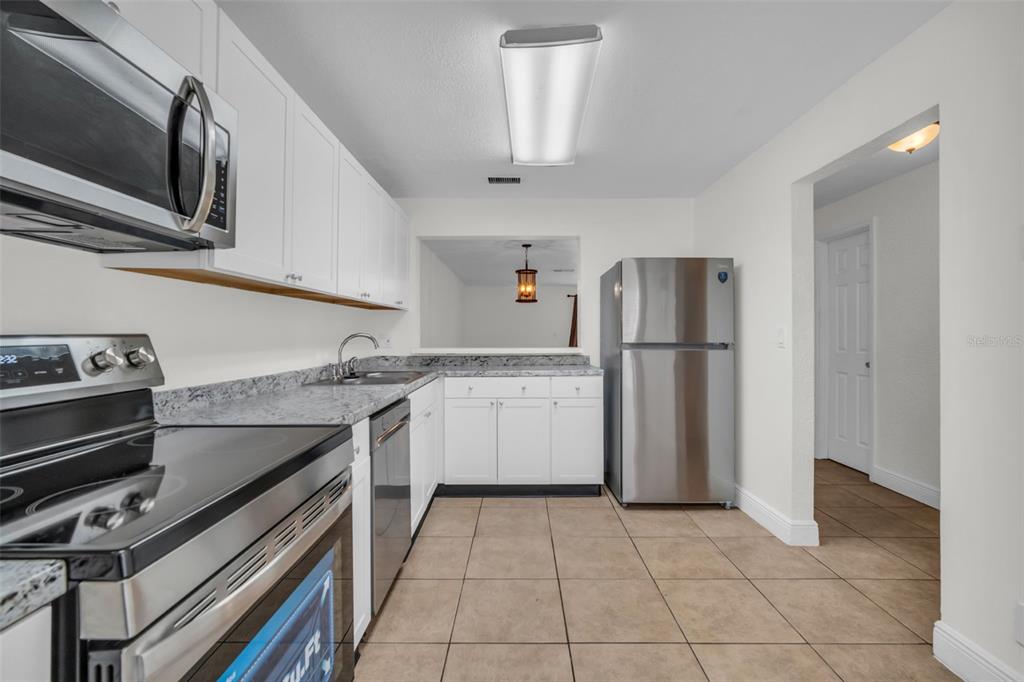 A kitchen features white cabinets, granite countertops, stainless steel appliances, and beige tile flooring — 1610 NW 93RD AVENUE UNIT 303, HOLLYWOOD, FL