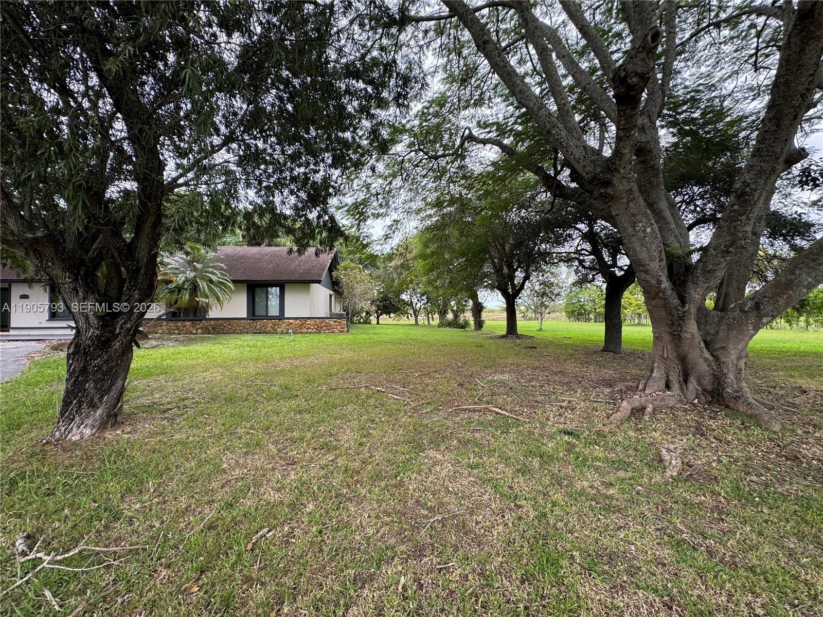 A grassy yard features large mature trees in front of a single-story house — 18750 SW 207th Ave, Miami FL 33187, MIAMI, FL