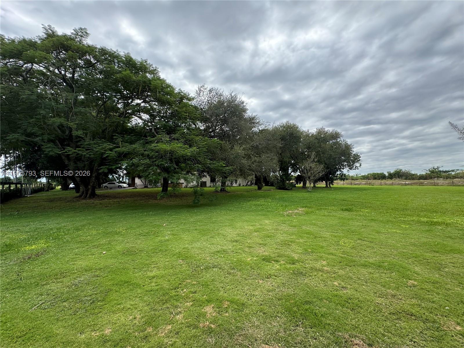 A large, grassy yard features several mature trees under a cloudy sky — 18750 SW 207th Ave, Miami FL 33187, MIAMI, FL