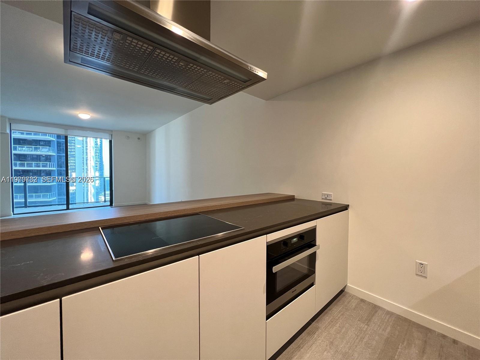 A modern kitchen features white cabinets, a dark countertop, a cooktop, and a range hood — 1000 Brickell Plz # 3503, Miami FL 33131, MIAMI, FL