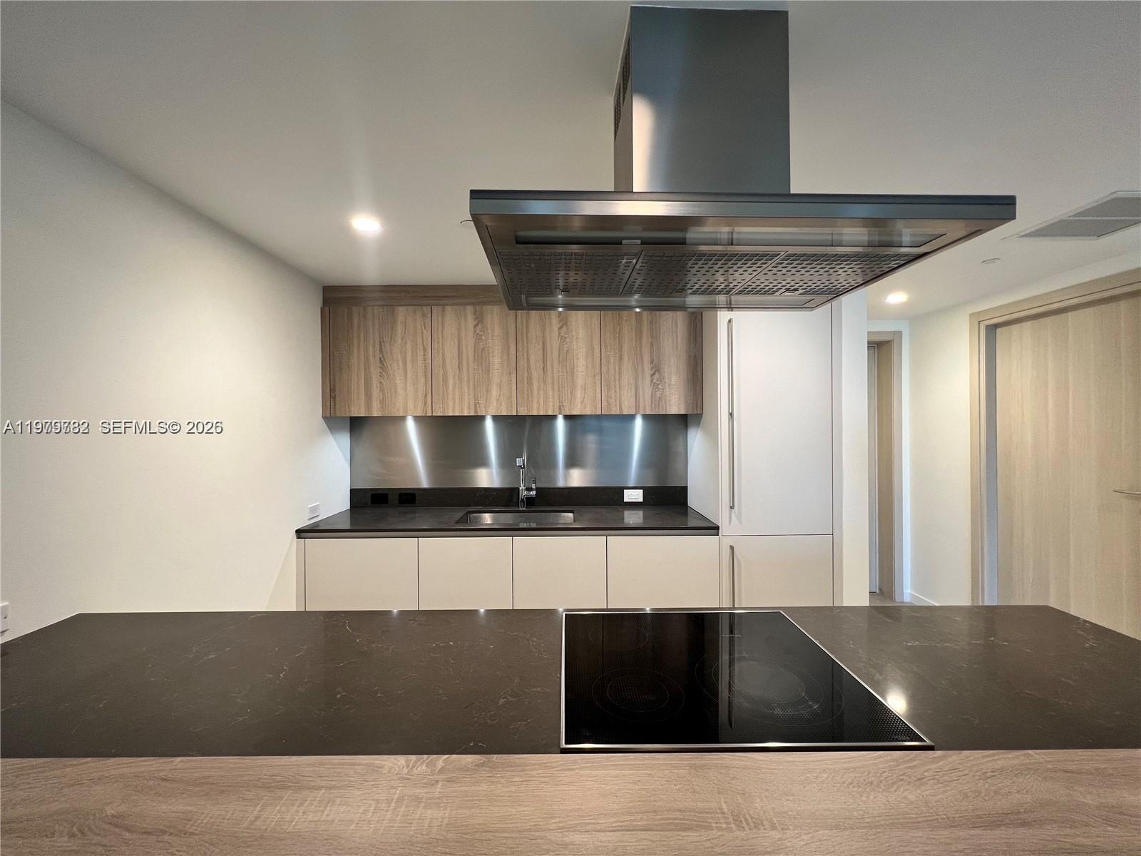 A modern kitchen features a dark countertop island with a cooktop and wood-toned cabinetry — 1000 Brickell Plz # 3503, Miami FL 33131, MIAMI, FL