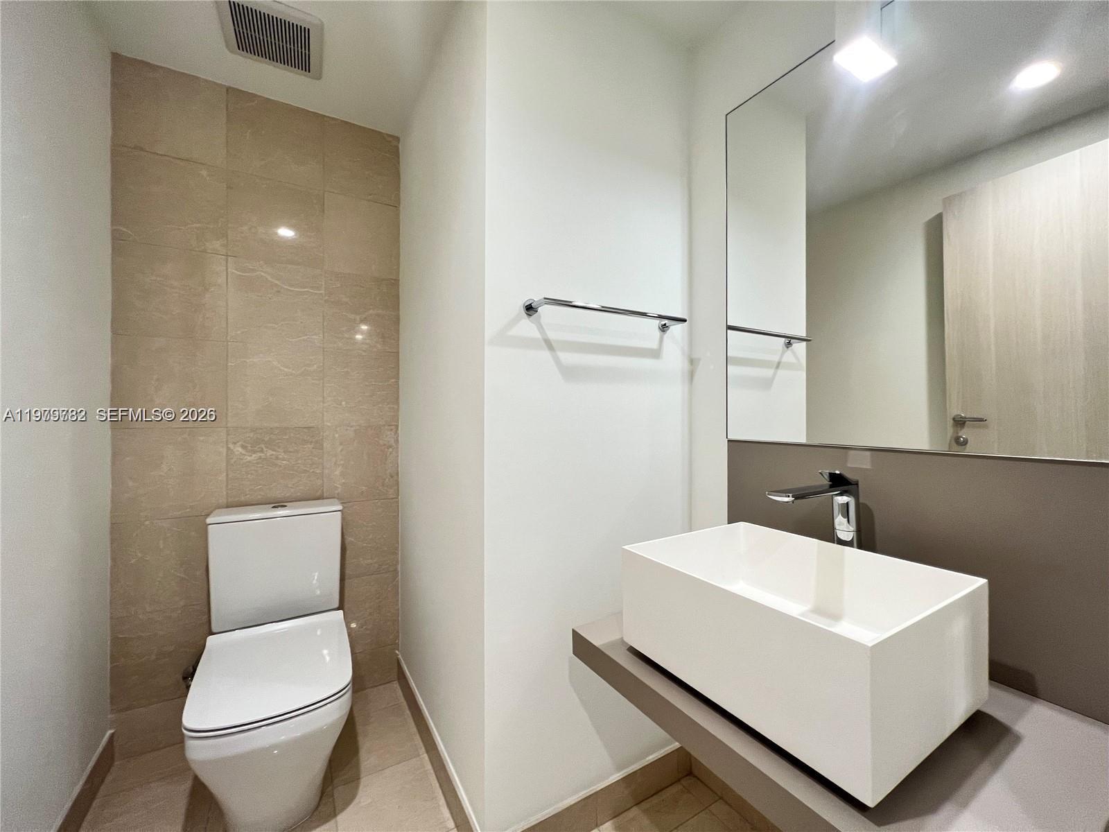A modern bathroom features a white vessel sink, a wall-mounted toilet, and beige tiling — 1000 Brickell Plz # 3503, Miami FL 33131, MIAMI, FL