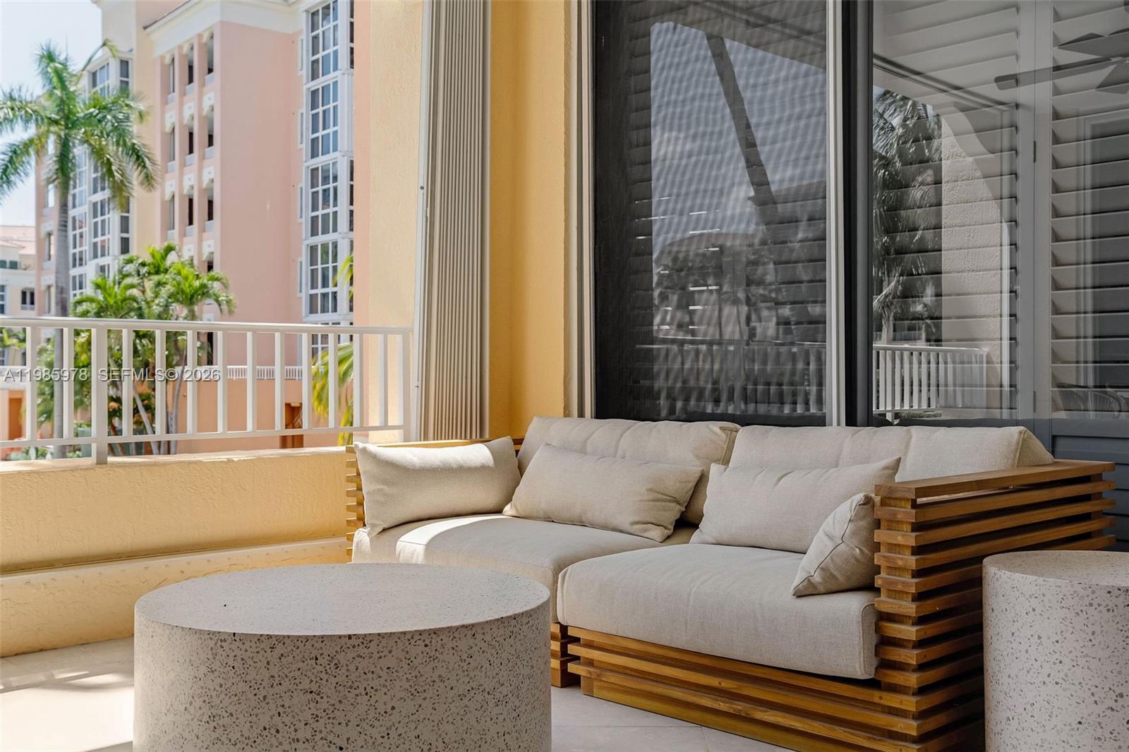 A beige outdoor sofa and two stone tables sit on a balcony with palm trees — 725 Crandon Blvd # 203, Key Biscayne FL 33149, KEY BISCAYNE, FL