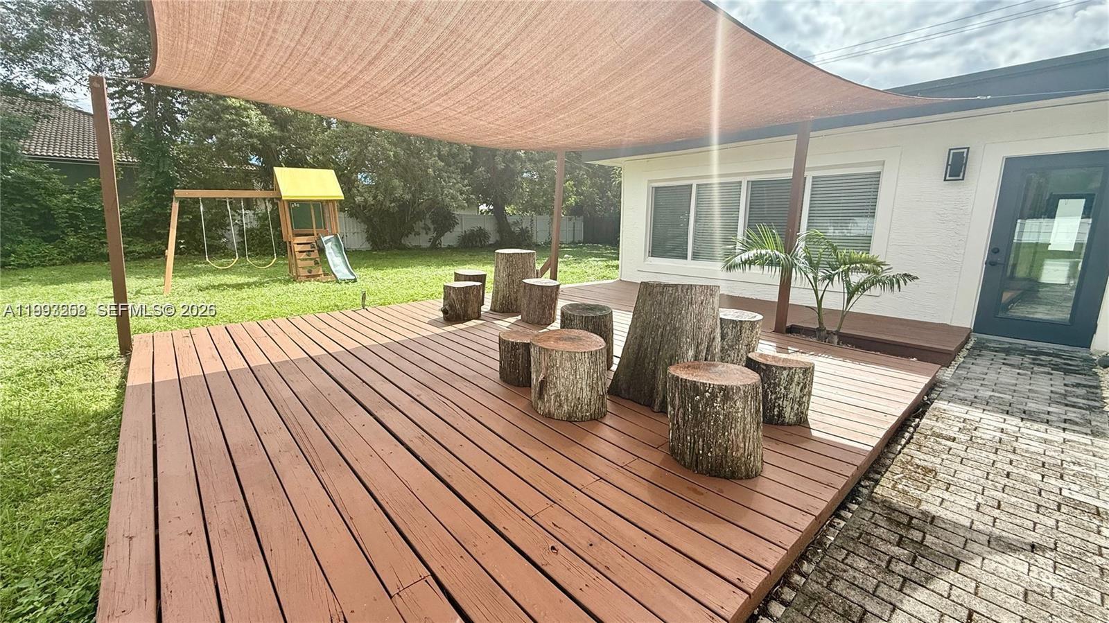 A wooden deck features tree stump seating under a shade sail in a backyard — 5401 W Broward Blvd, Plantation FL 33317, PLANTATION, FL