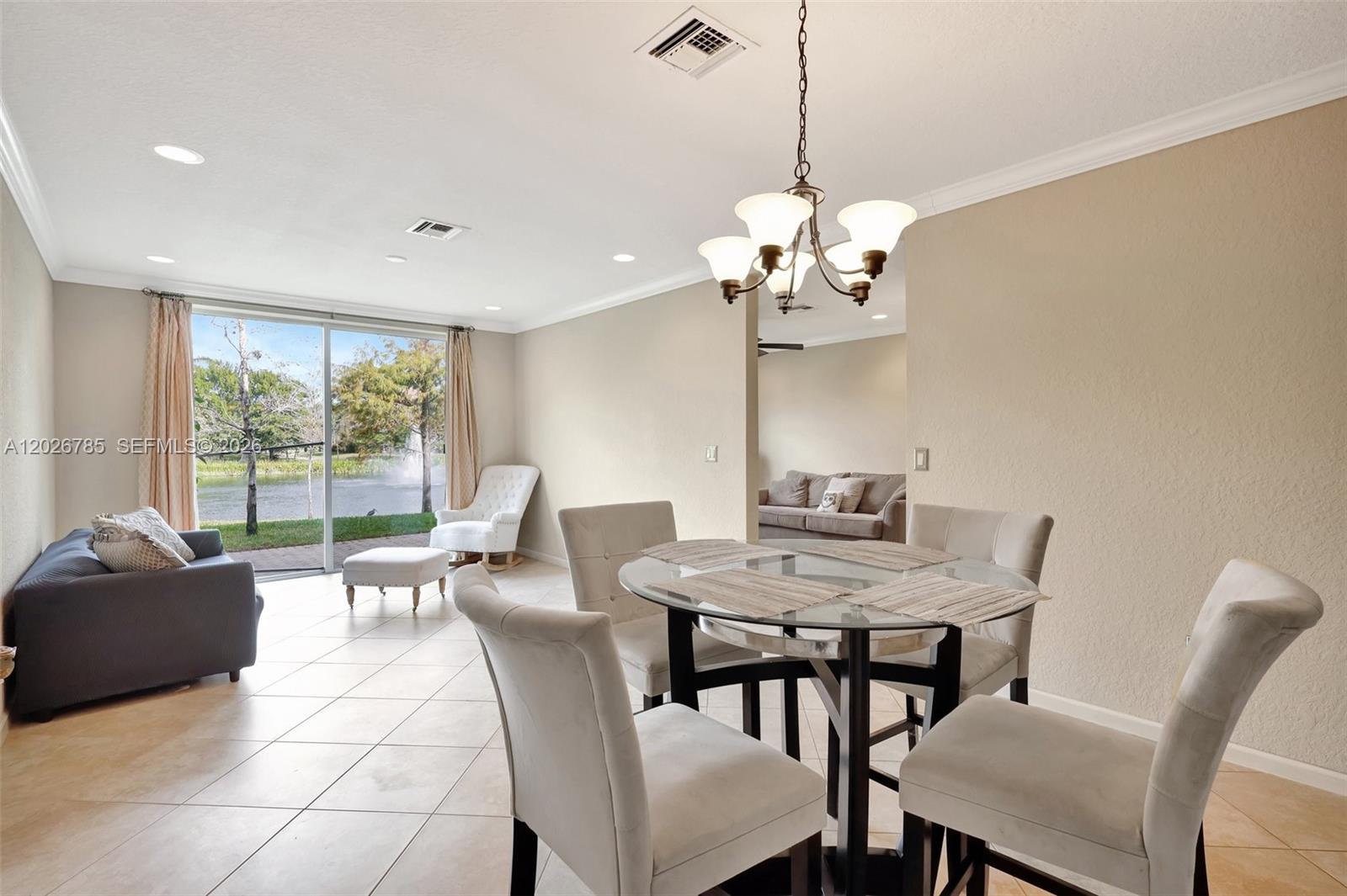 A dining area with a glass table and chairs overlooks a lake through sliding doors — 4302 Colony View Dr, Lake Worth FL 33463, LAKE WORTH, FL