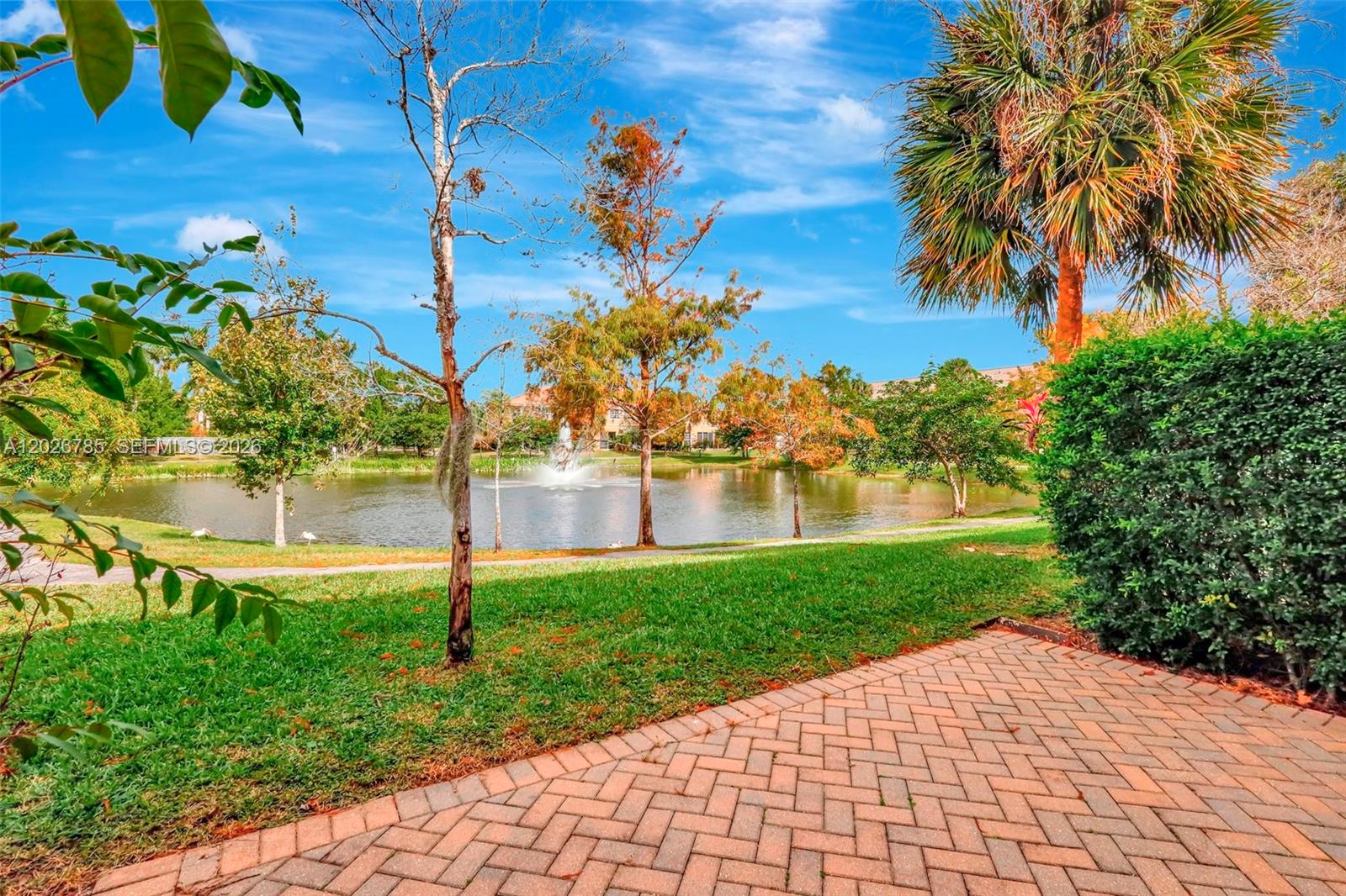 A paved patio overlooks a grassy lawn, a pond with a fountain, and trees — 4302 Colony View Dr, Lake Worth FL 33463, LAKE WORTH, FL
