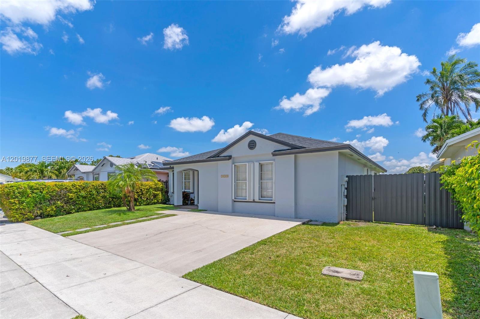 A single-story gray house features a concrete driveway, a front lawn, and a side fence — 13520 SW 180th Ter, Miami FL 33177, MIAMI, FL