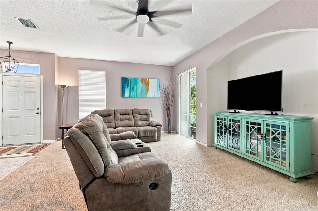 A living room features a light blue media console, brown reclining furniture, and a ceiling fan — 8421 SHALLOW CREEK COURT, NEW PORT RICHEY, FL