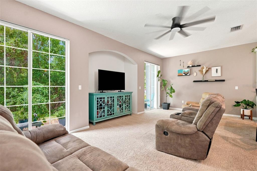 A living room features a teal media console, brown reclining furniture, and large sliding glass doors — 8421 SHALLOW CREEK COURT, NEW PORT RICHEY, FL