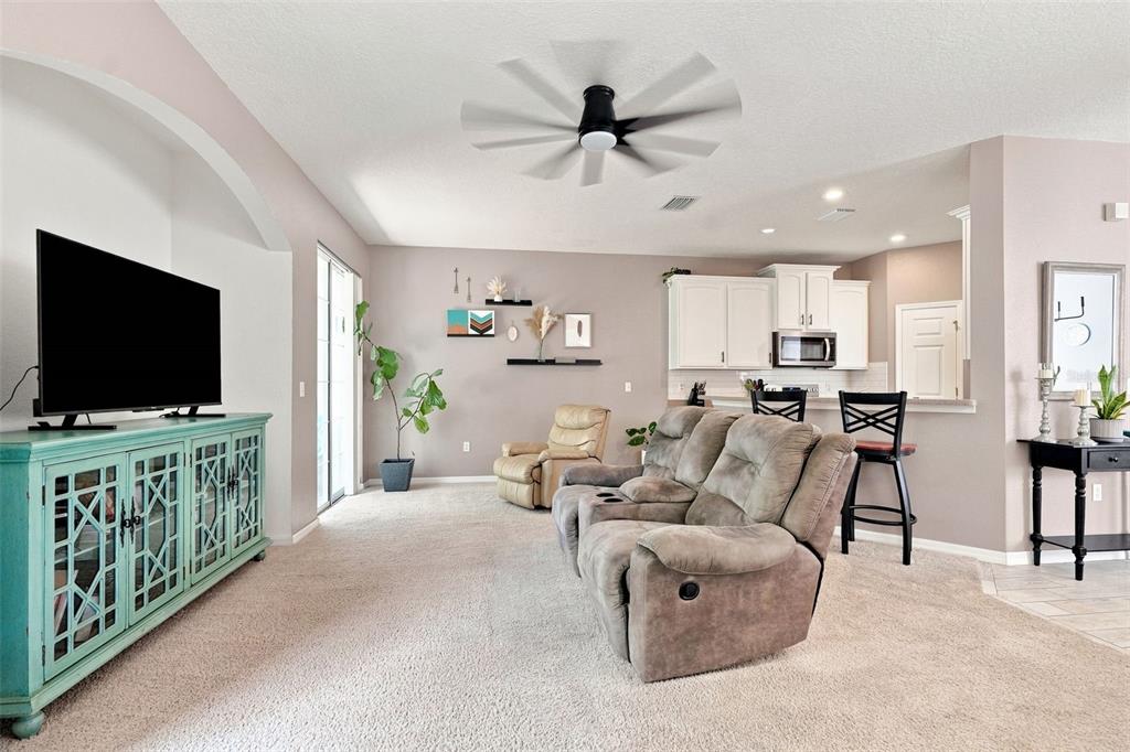This living room features a teal media console, a reclining sofa, and an open kitchen — 8421 SHALLOW CREEK COURT, NEW PORT RICHEY, FL