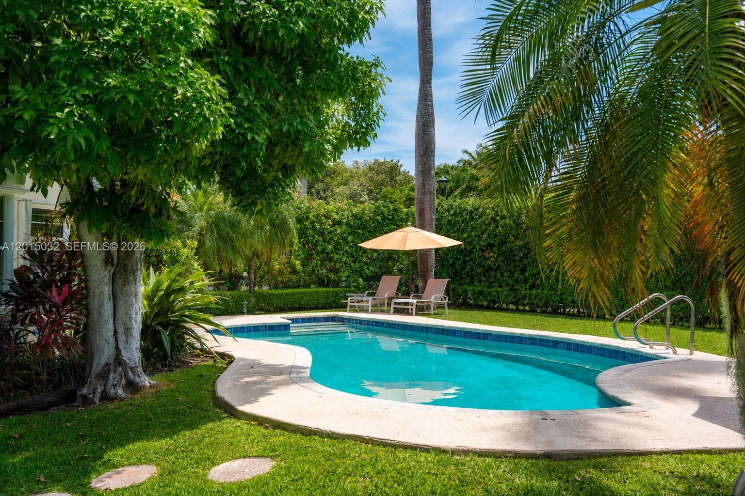 A swimming pool with a patio and umbrella is surrounded by a tall hedge — 363 S Hibiscus Dr, Miami Beach FL 33139, MIAMI BEACH, FL