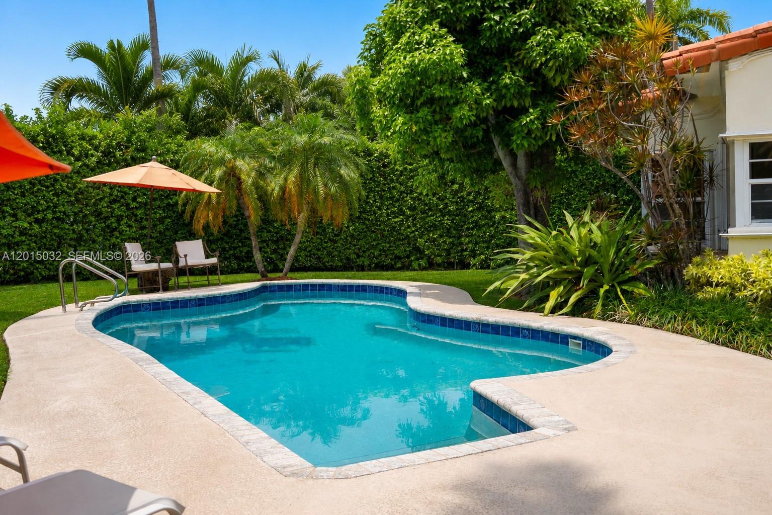 A backyard swimming pool with a patio, orange umbrellas, and lush landscaping — 363 S Hibiscus Dr, Miami Beach FL 33139, MIAMI BEACH, FL