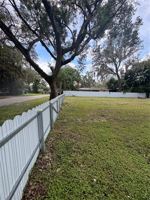 A white metal fence borders a grassy lot with large trees under a cloudy sky — 2211 KEUKA AVENUE, LEESBURG, FL