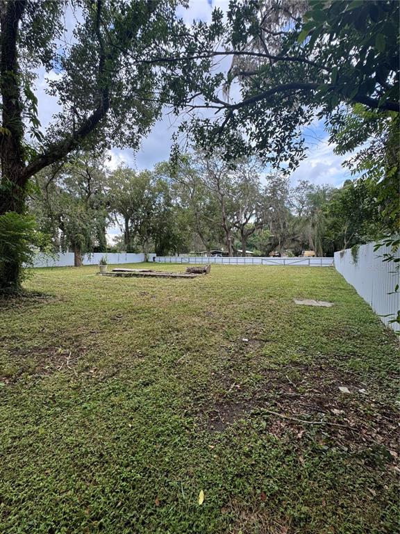 A large, grassy backyard is enclosed by a white fence and shaded by mature trees — 2211 KEUKA AVENUE, LEESBURG, FL