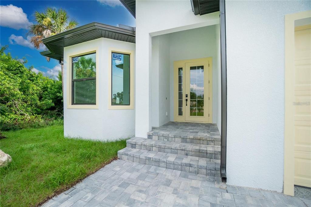 A white house exterior features a paved walkway, three stone steps, and a yellow-framed door — 289 ALBATROSS ROAD, ROTONDA WEST, FL