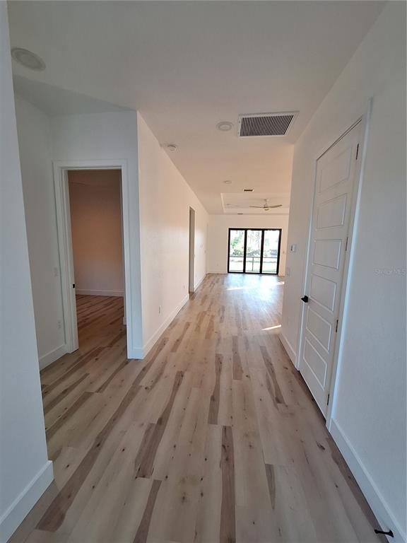 A hallway with light wood-look flooring leads toward a living area with glass sliding doors — 289 ALBATROSS ROAD, ROTONDA WEST, FL