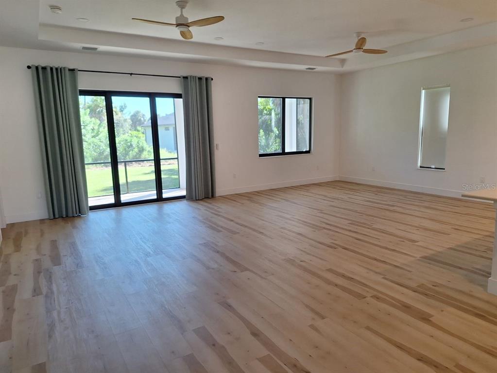 A spacious, empty living room features light wood flooring, two ceiling fans, and sliding glass doors — 289 ALBATROSS ROAD, ROTONDA WEST, FL