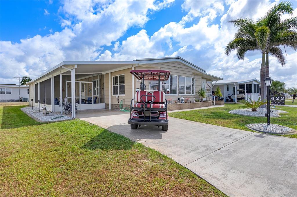 A single-story mobile home with a screened porch, concrete driveway, and a golf cart — 622 LA SALA, NORTH PORT, FL