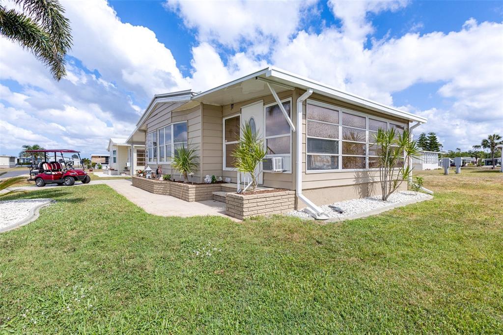 A tan mobile home with a screened-in porch, brick skirting, and a golf cart nearby — 622 LA SALA, NORTH PORT, FL