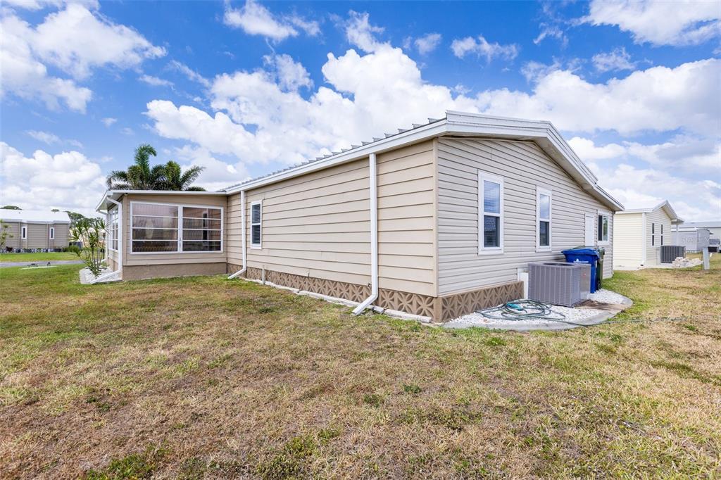 The exterior of a tan manufactured home features a screened-in porch and an air conditioning unit — 622 LA SALA, NORTH PORT, FL