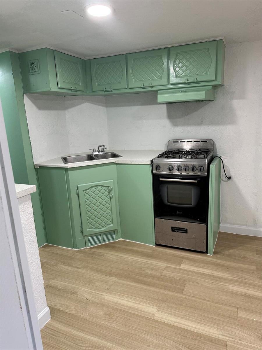 A small kitchen features green cabinets, a corner sink, a gas stove, and light wood flooring — 4361 Davis Road # 3, Lake Worth FL 33461, LAKE WORTH, FL