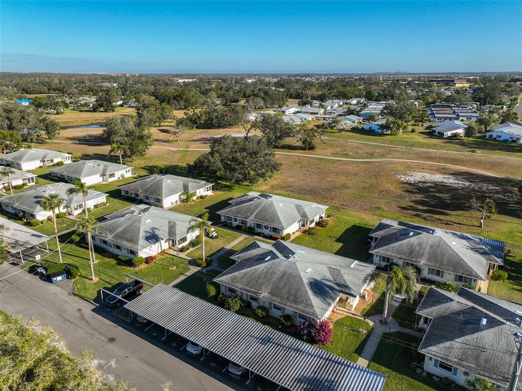 An aerial view shows several single-story residential buildings with covered parking and surrounding green space — 1901 CANTERBURY LANE UNIT 19, SUN CITY CENTER, FL