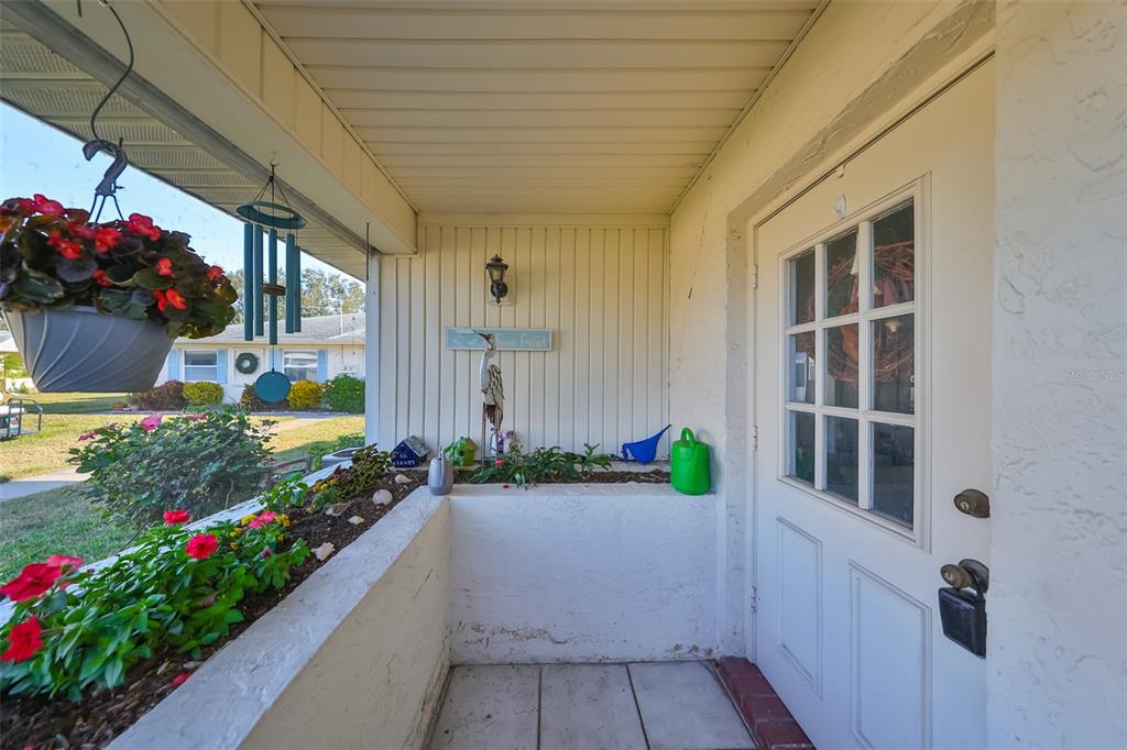 A covered front porch features a white door, a planter box, and hanging flower baskets — 1901 CANTERBURY LANE UNIT 19, SUN CITY CENTER, FL
