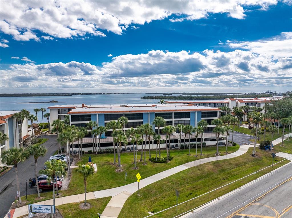 An aerial view shows a multi-story apartment complex with blue siding near a large body — 1551 BEACH ROAD UNIT 204, ENGLEWOOD, FL