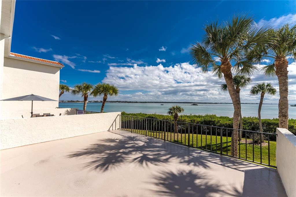 A spacious outdoor balcony overlooks a calm bay with palm trees and a blue sky — 1551 BEACH ROAD UNIT 204, ENGLEWOOD, FL