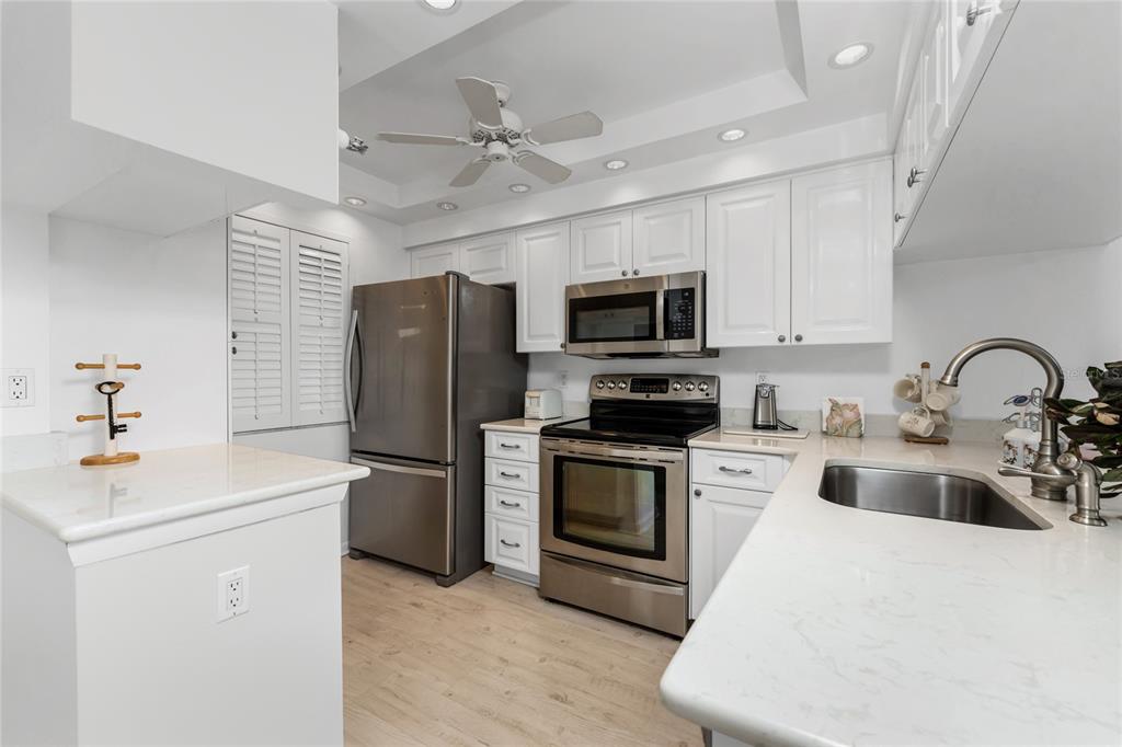 A kitchen features white cabinets, stainless steel appliances, and light countertops with a ceiling fan — 1551 BEACH ROAD UNIT 204, ENGLEWOOD, FL