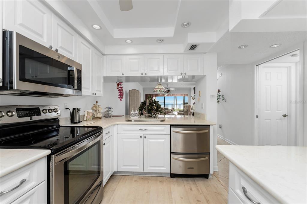 A kitchen features white cabinets, stainless steel appliances, and a view into a living area — 1551 BEACH ROAD UNIT 204, ENGLEWOOD, FL