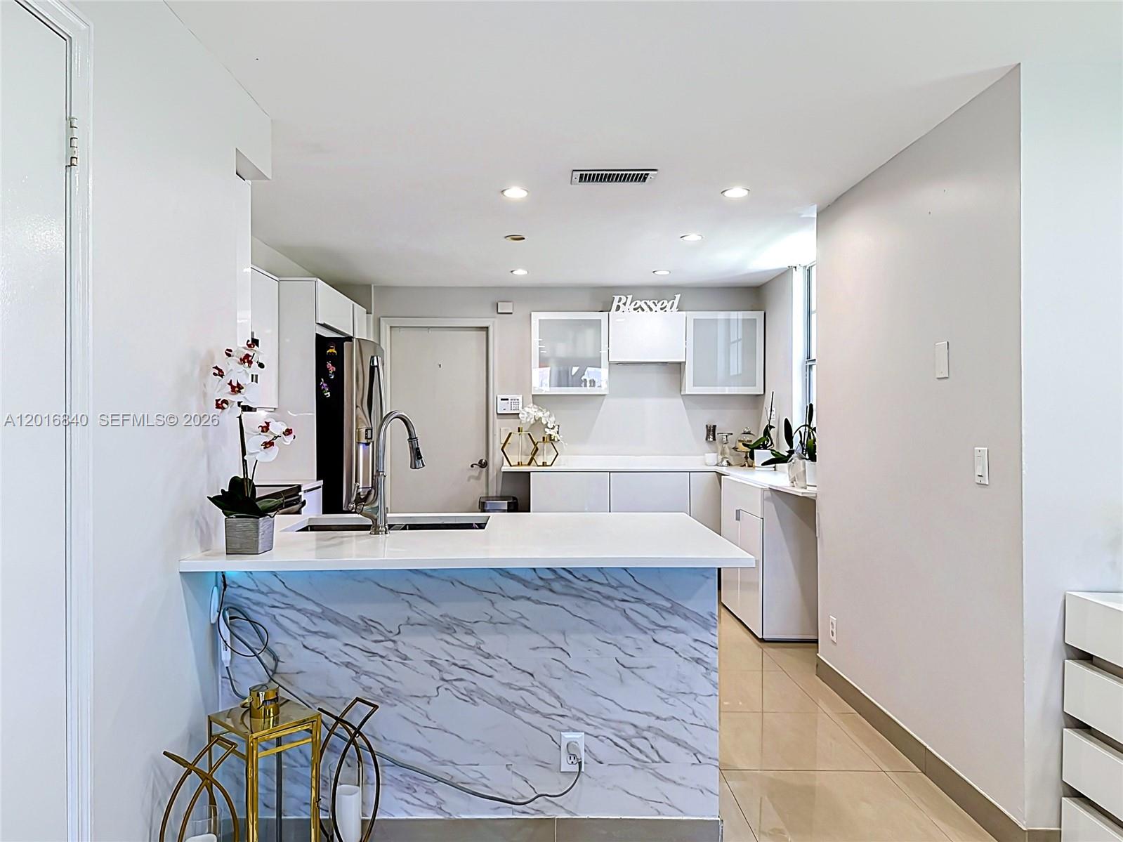 A modern kitchen features a marble-patterned island, white cabinetry, and light-colored tile flooring — 952 Sevilla Cir, Weston FL 33326, WESTON, FL